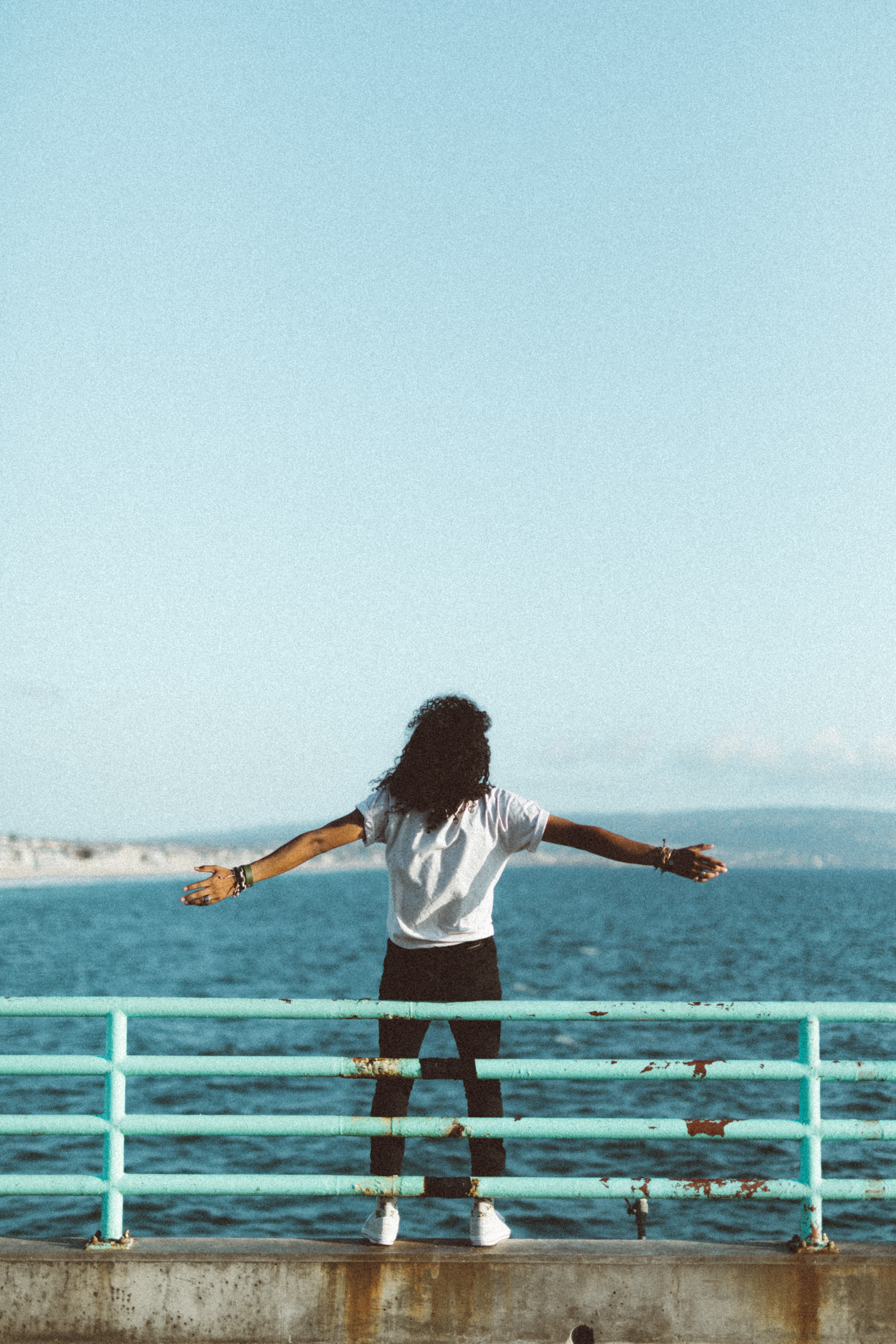 Woman gazing out at ocean with arms open.
